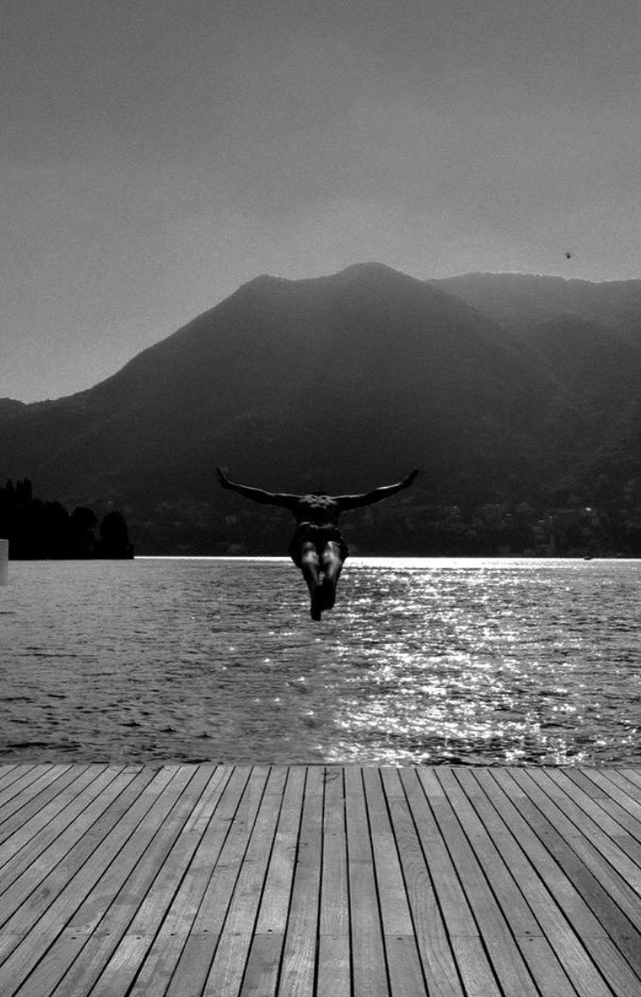 Man jumping from wooden dock with mountains in the background in black and white