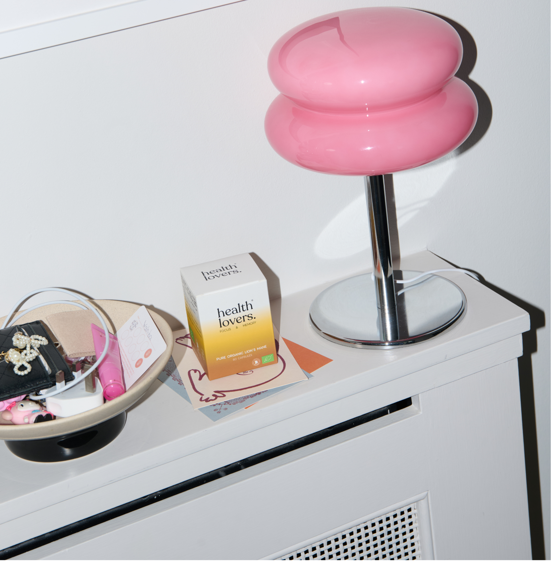 Pink stool on a white surface with a box and small items nearby, framed picture in the background.