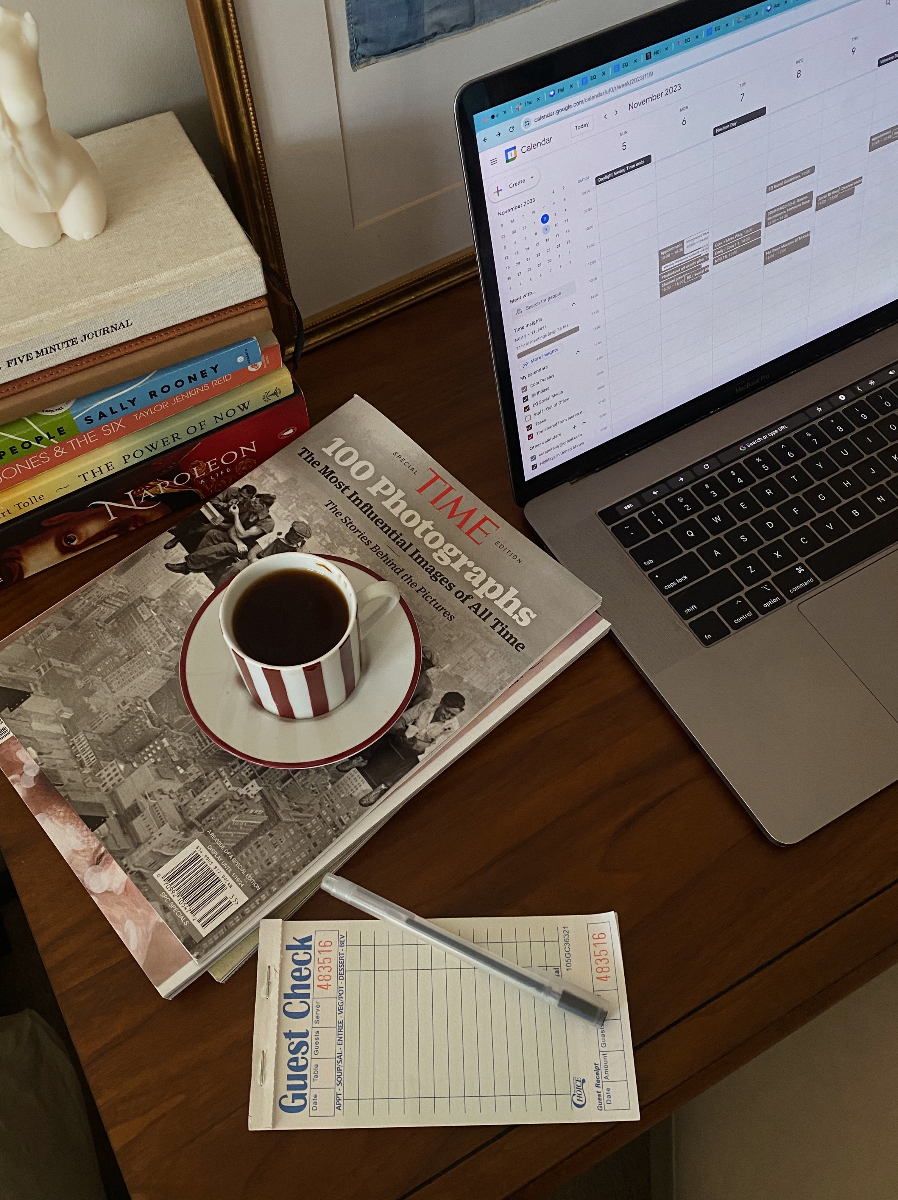 Laptop on a desk with a cup of coffee, books, and a magasine.