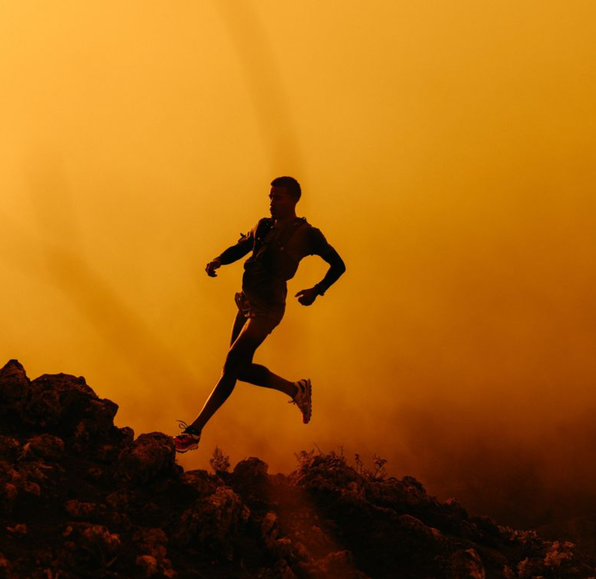 Silhouette of a person running on a rocky landscape with a warm, orange sky.
