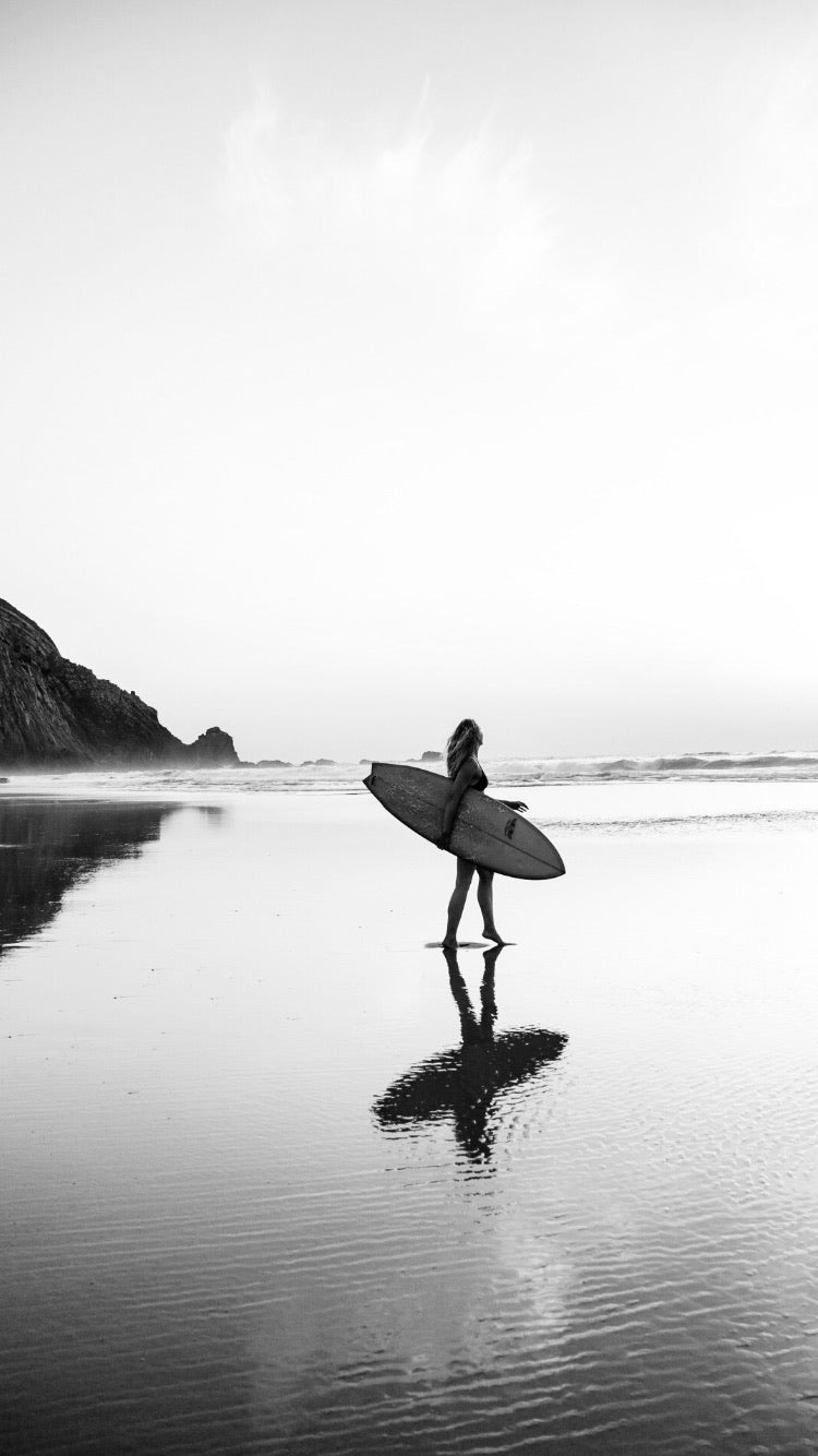 Person holding a surfboard on a beach with a mountain in the background
